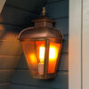 Wandlamp koper met bronzen vlam bovenop hangend aan een saunahuisje.